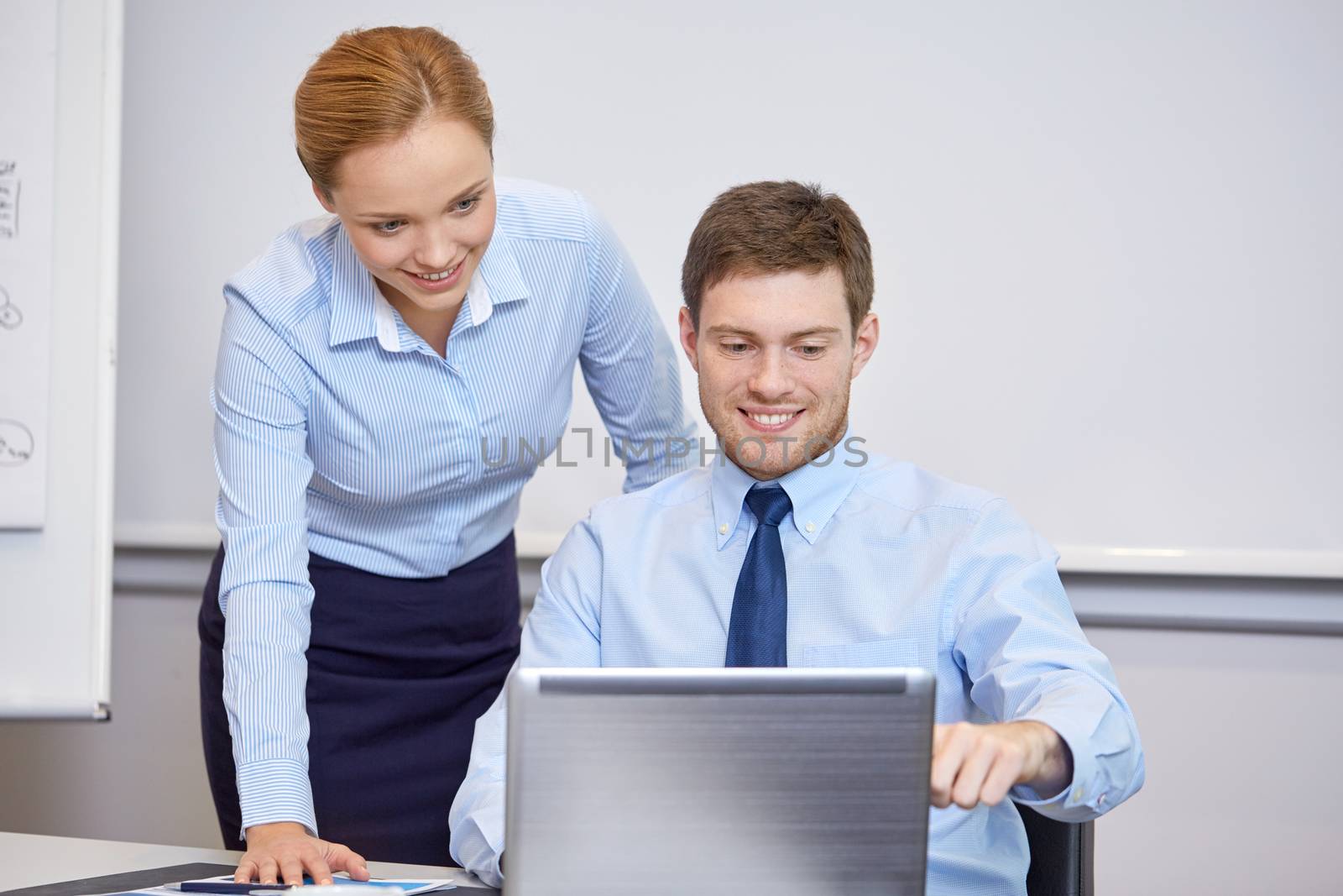 smiling businesspeople with laptop in office by dolgachov