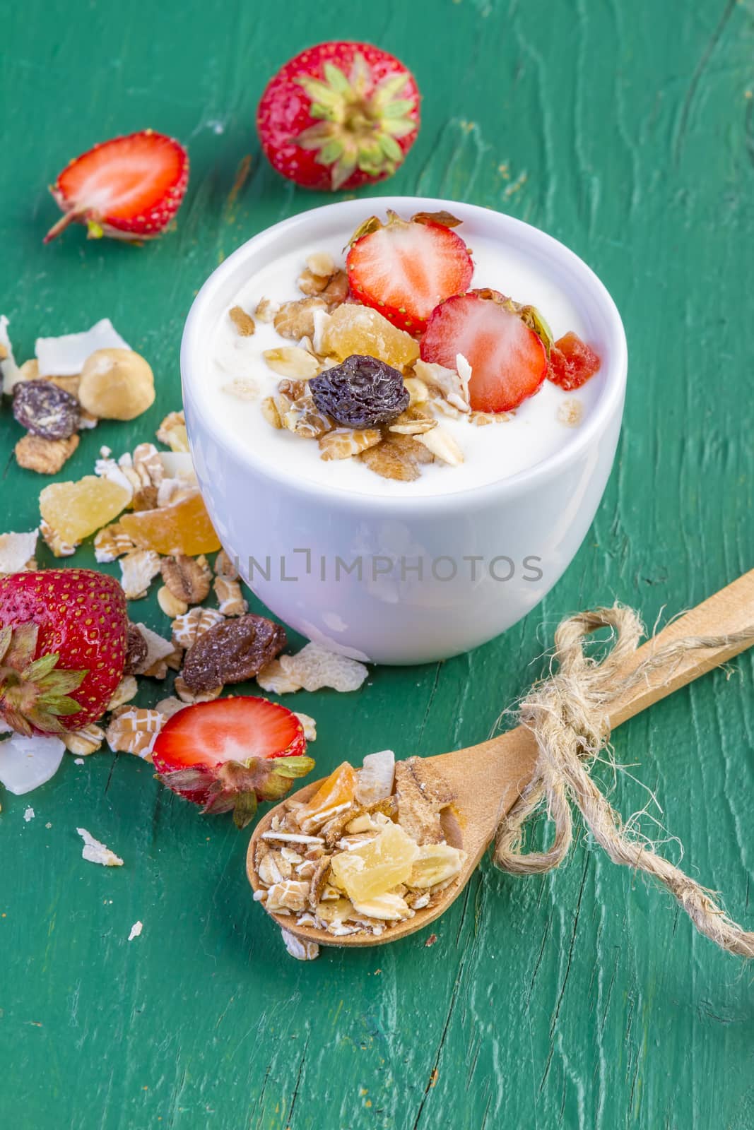 yogurt with cereals muesli, fresh strawberries, banana and raisins in bowl on wooden background