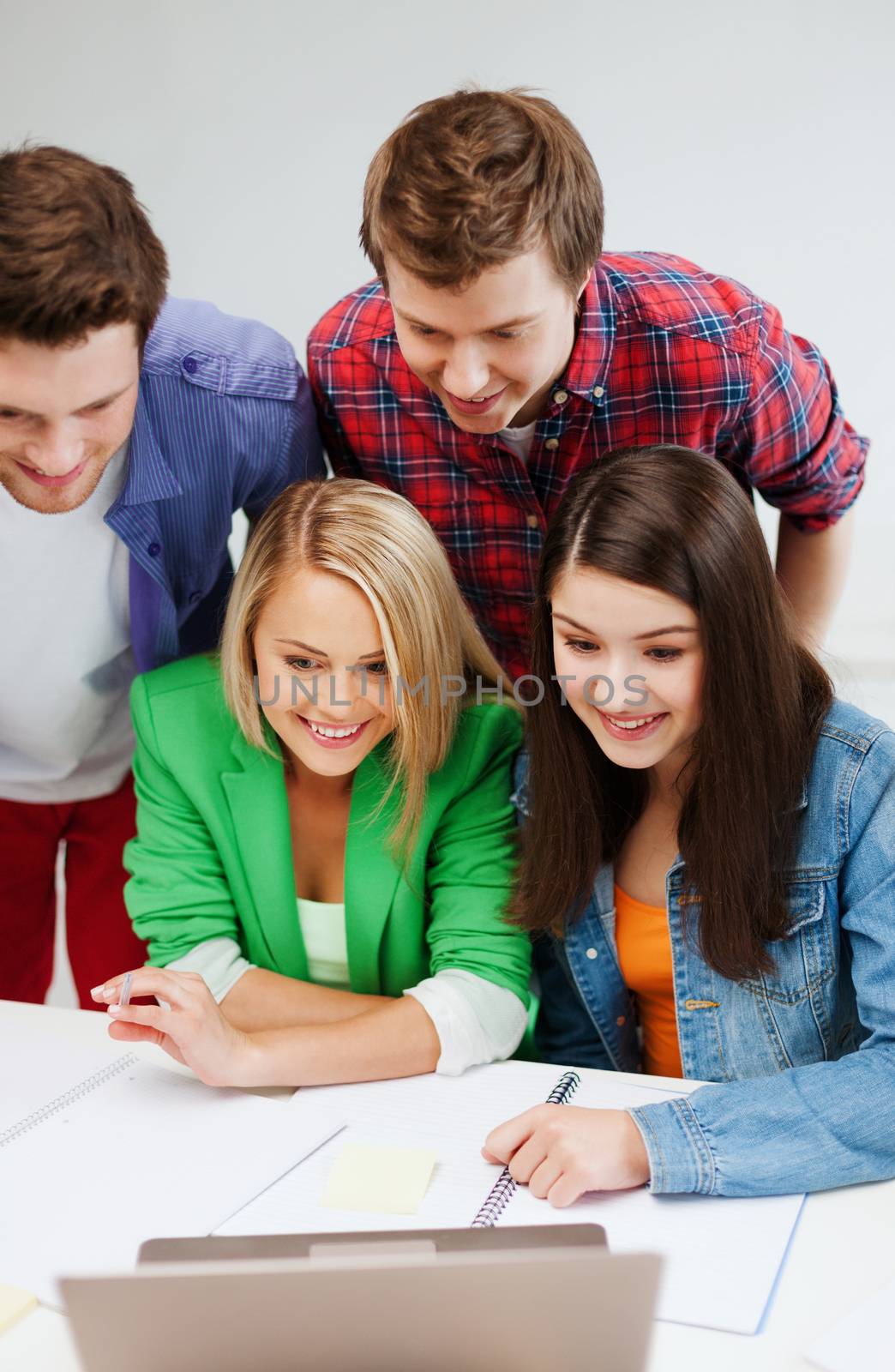 education concept - smiling students looking at laptop at school