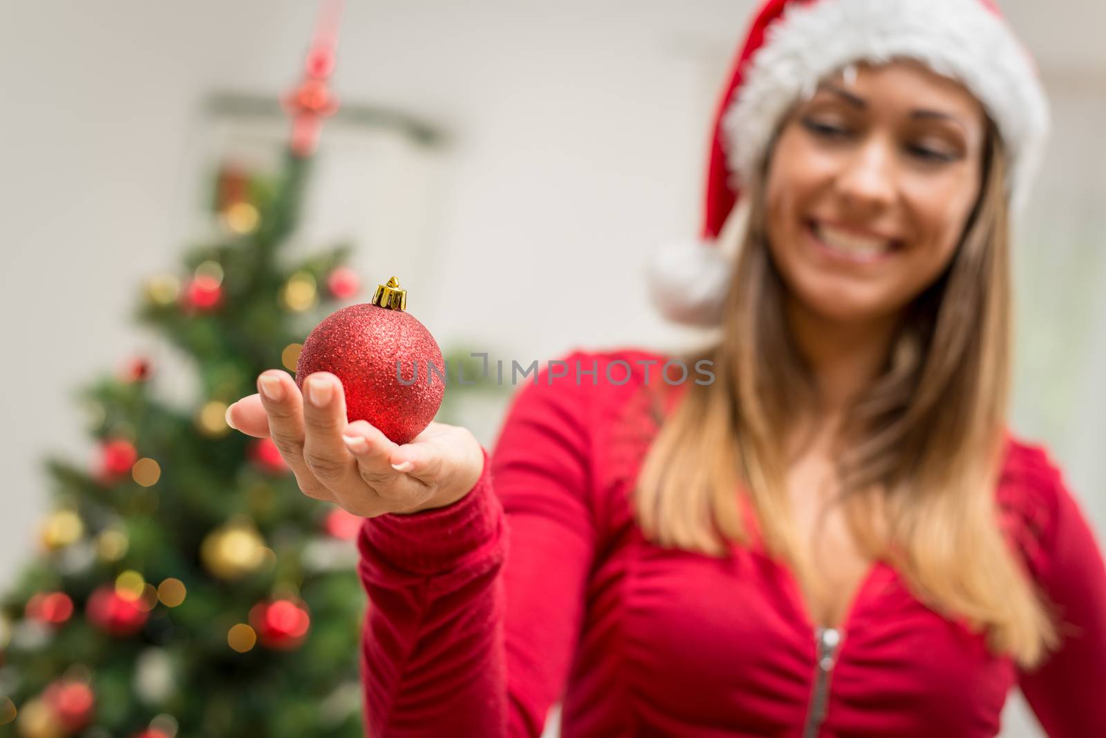 Close-up of a happy beautiful young woman holding red Christmas ornament. Selective focus. Focus on ornament in foreground.