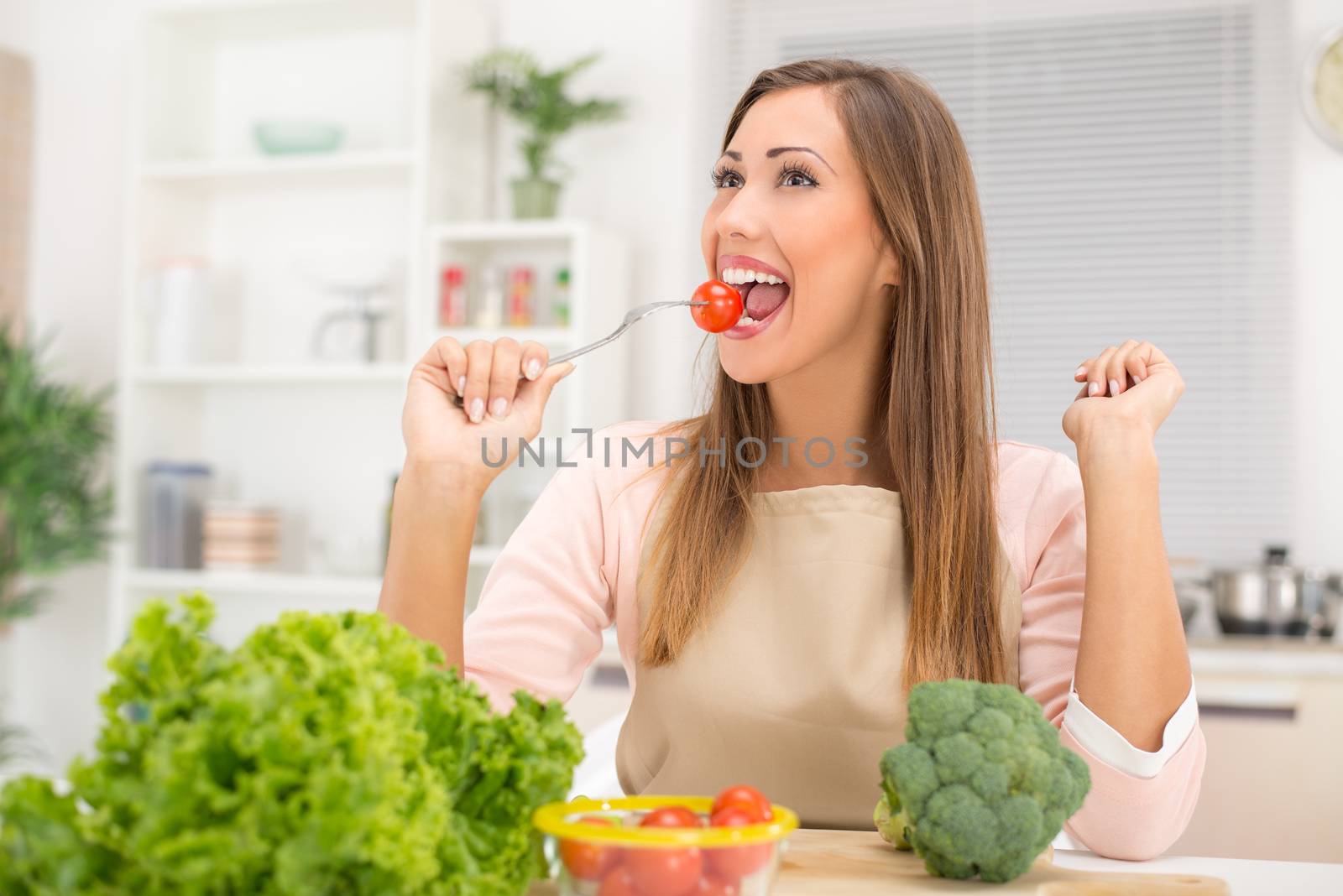 Beautiful young woman in the kitchen eating red cherry tomato.