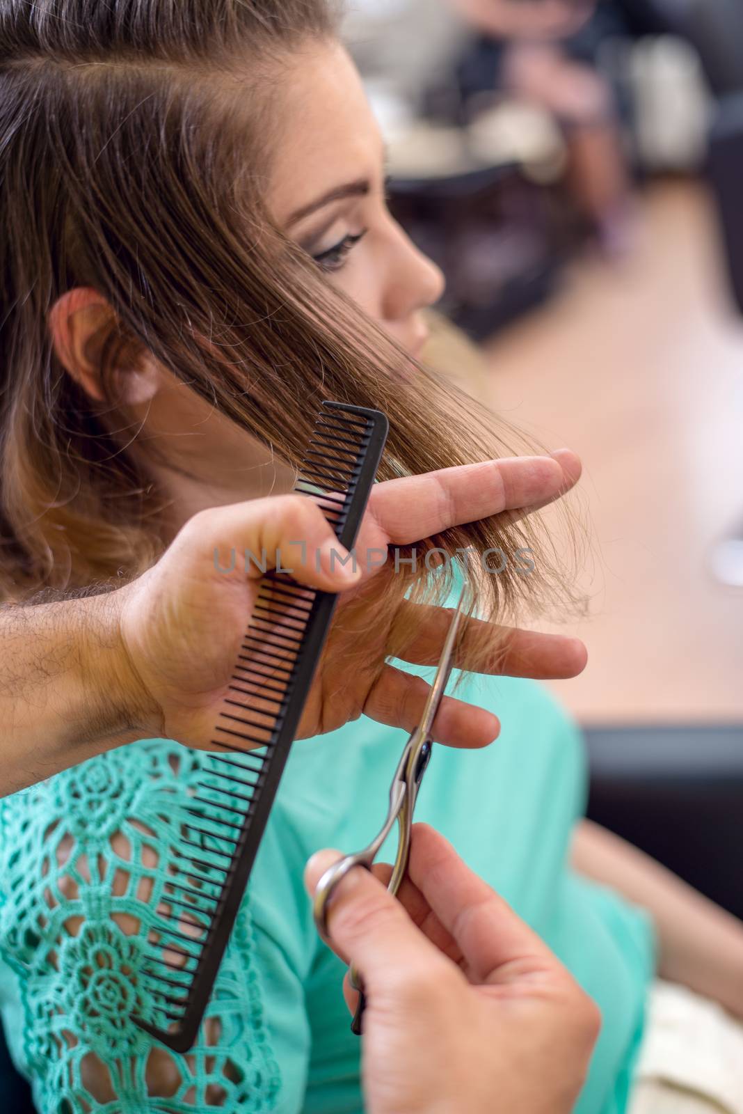 Close-up of a young beautiful woman having cut her hair at the man hairdresser.