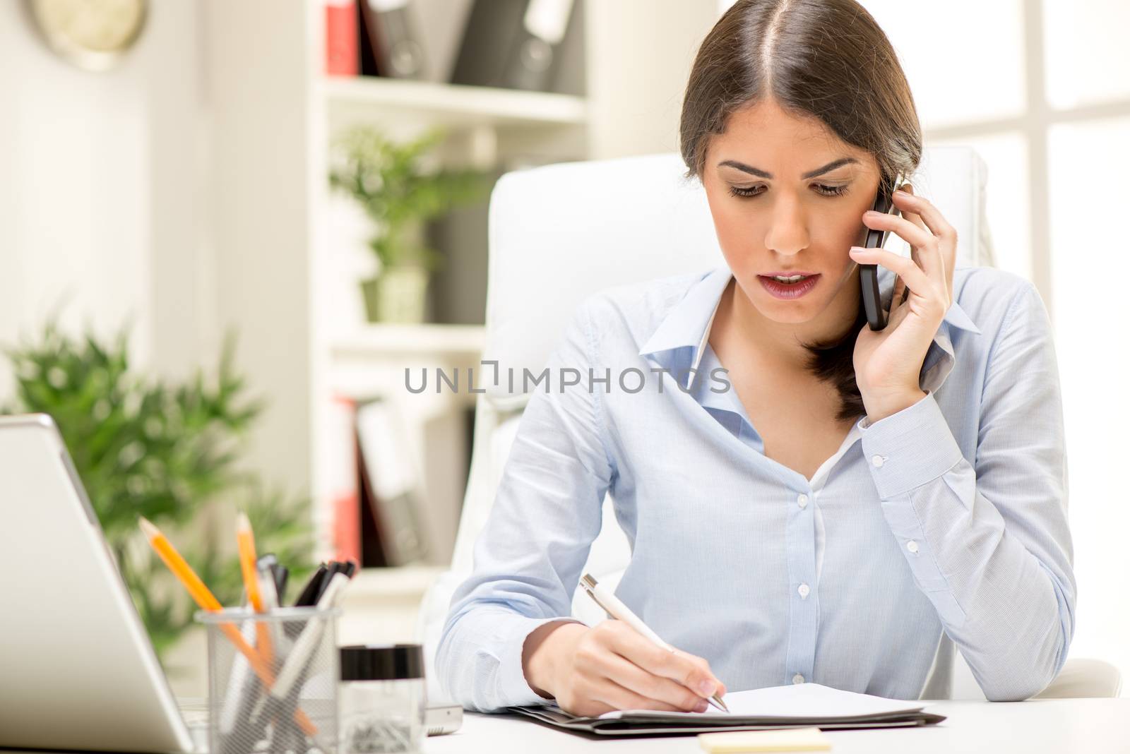 A young thinking businesswoman phoning with smart phone in office.
