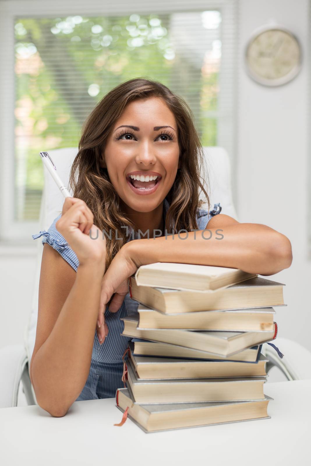 Cheerful teenage girl sitting in library with stack of books. 