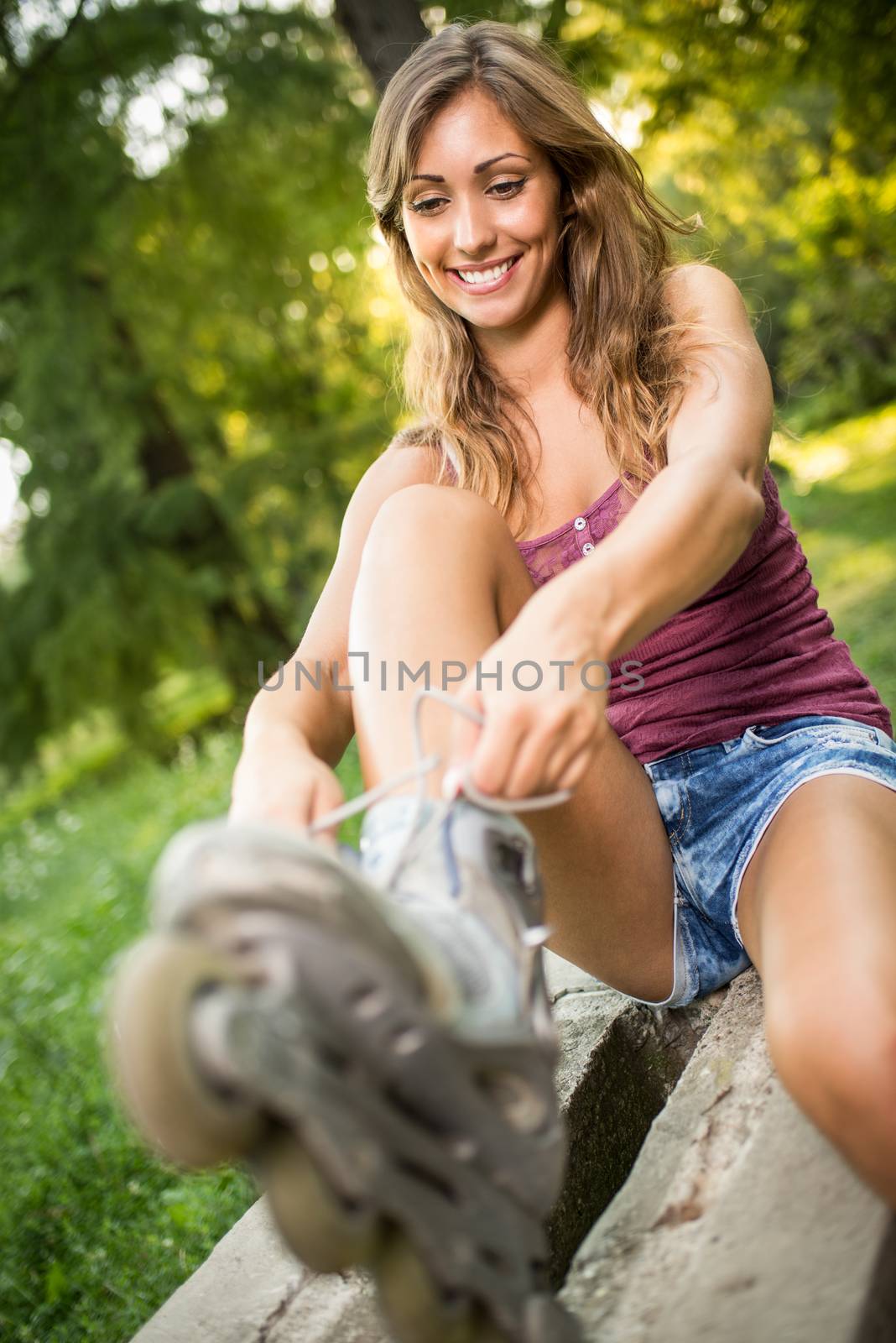 Young female skater sitting in the park and ties her rollers. Selective focus. 