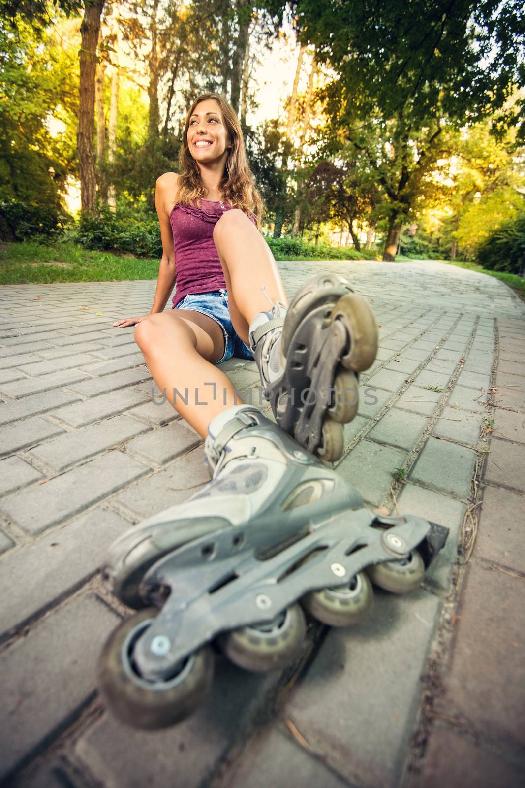 Beautiful girl roller sitting on track in the park and resting after roller skating.