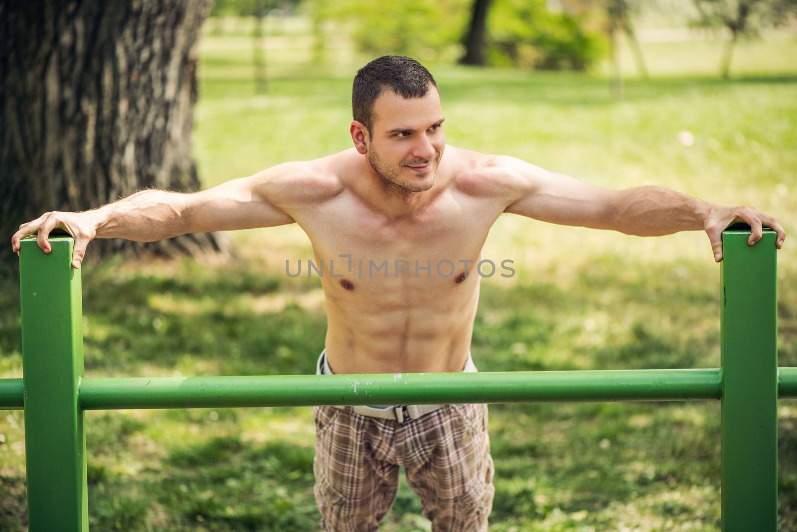 Naked muscle man resting after exercising in the outdoor gym.