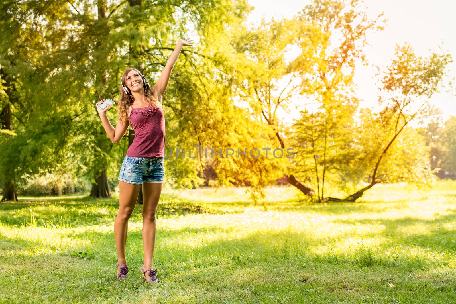 Happy beautiful girl enjoying music on headphones in the sunny park. 