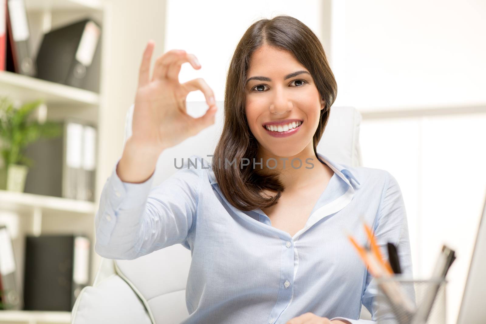 Successful businesswoman sitting at the desk in the office and showing okay sign.