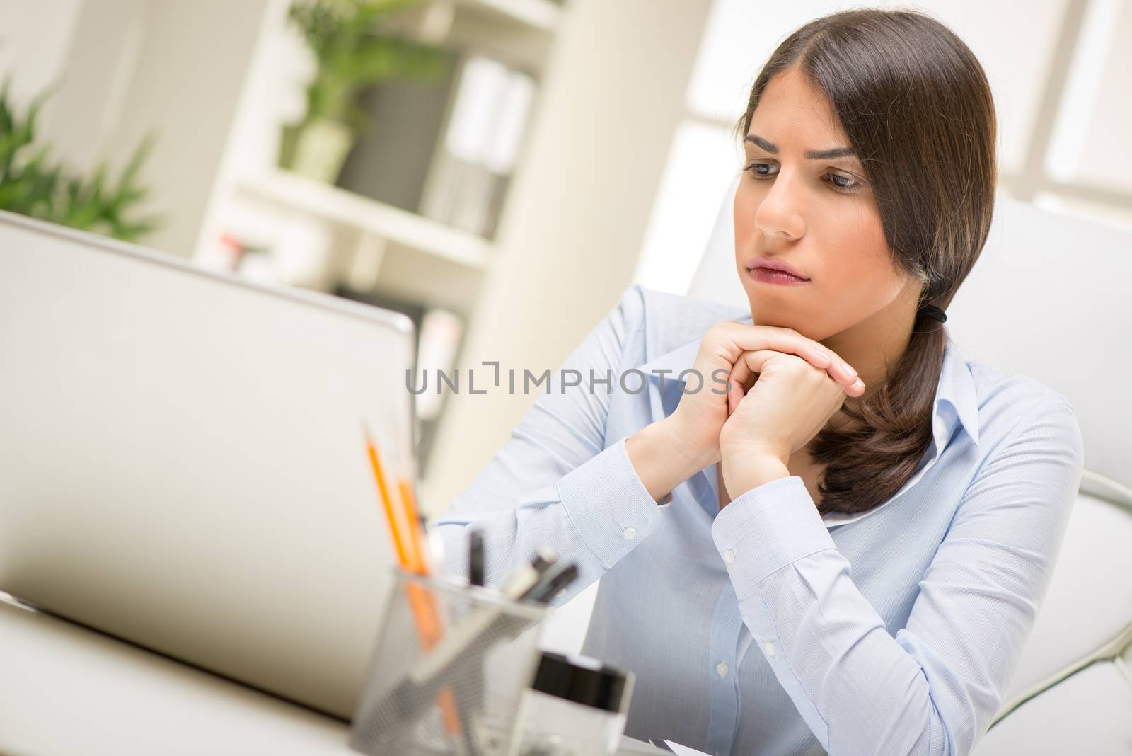 Portrait of a thinking businesswoman sitting in the office and looking at laptop.