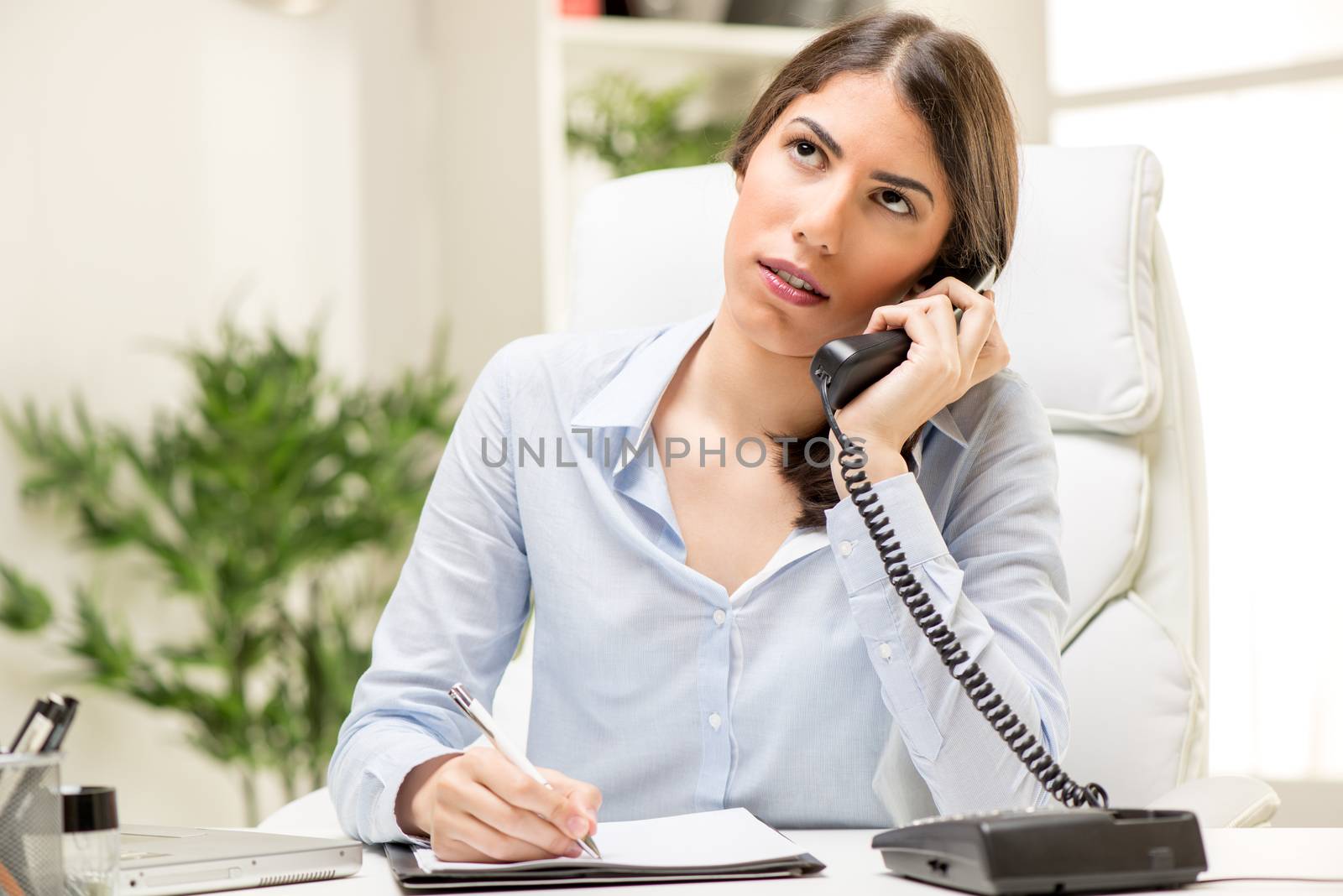 A young thinking businesswoman phoning in office