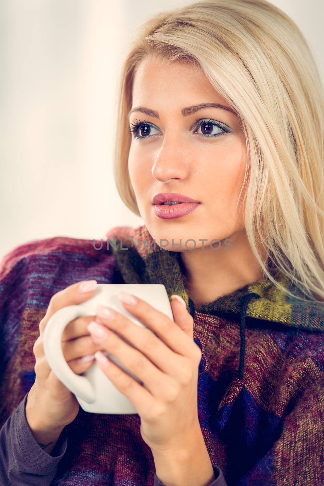 Beautiful blonde girl sits tucked, thinking and holding a cup of tea.