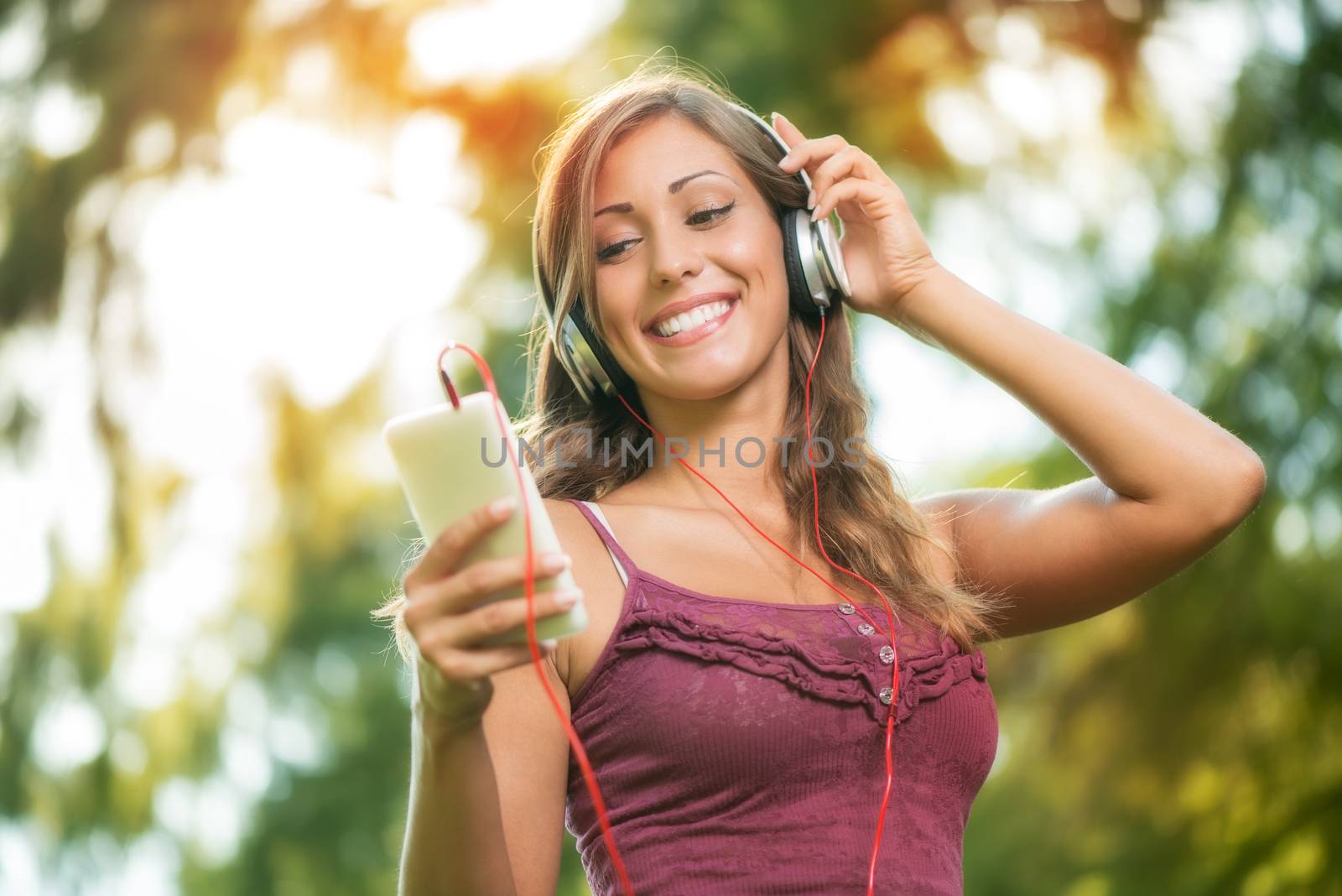 Happy beautiful girl in the park and listening music from smart phone.