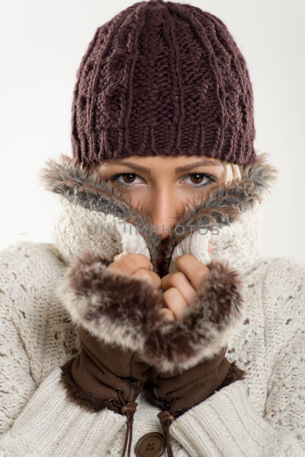 Beautiful young girl In winter clothes with a wool cap and fur gloves, sticks to the fur collar In which is tucking. Looking at camera.