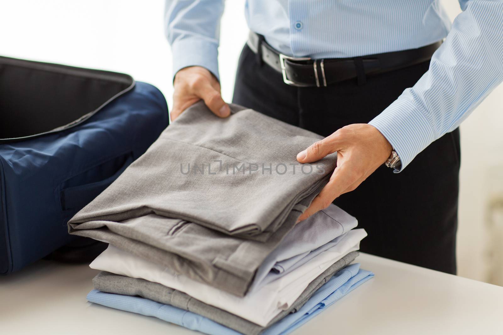 business, trip, luggage and people concept - close up of businessman packing clothes into travel bag
