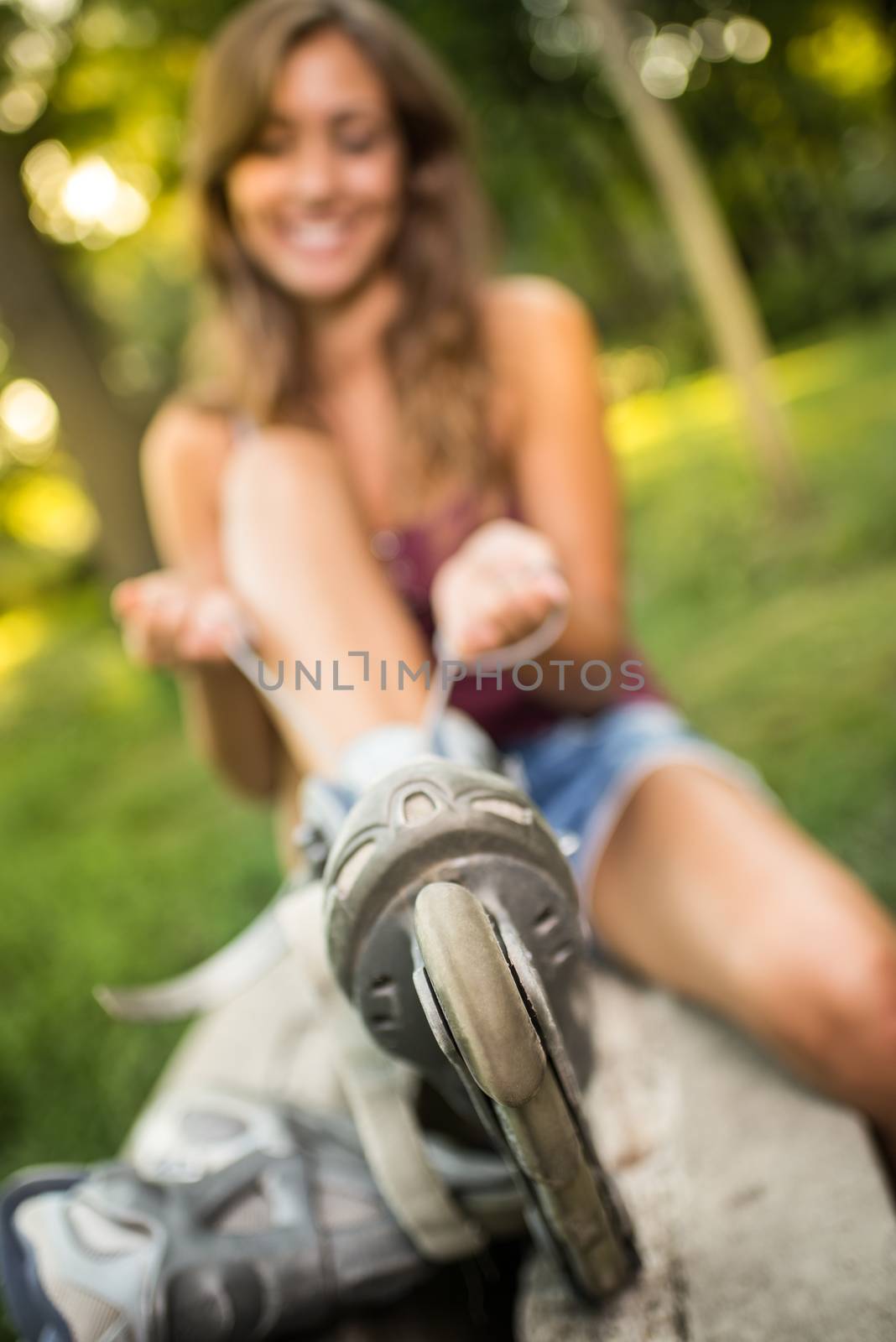 Young female skater sitting in the park and ties her rollers. Selective focus. Focus on Rollerblades. 