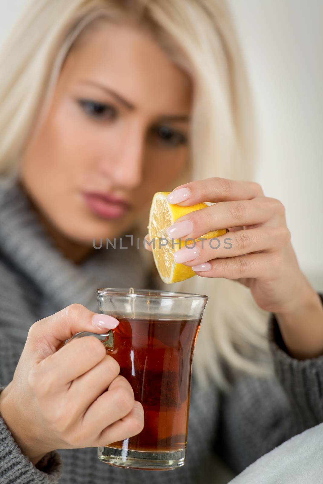 Beautiful girl with face out of focus squeezed lemon in a cup of tea. In the foreground are tea and lemon.