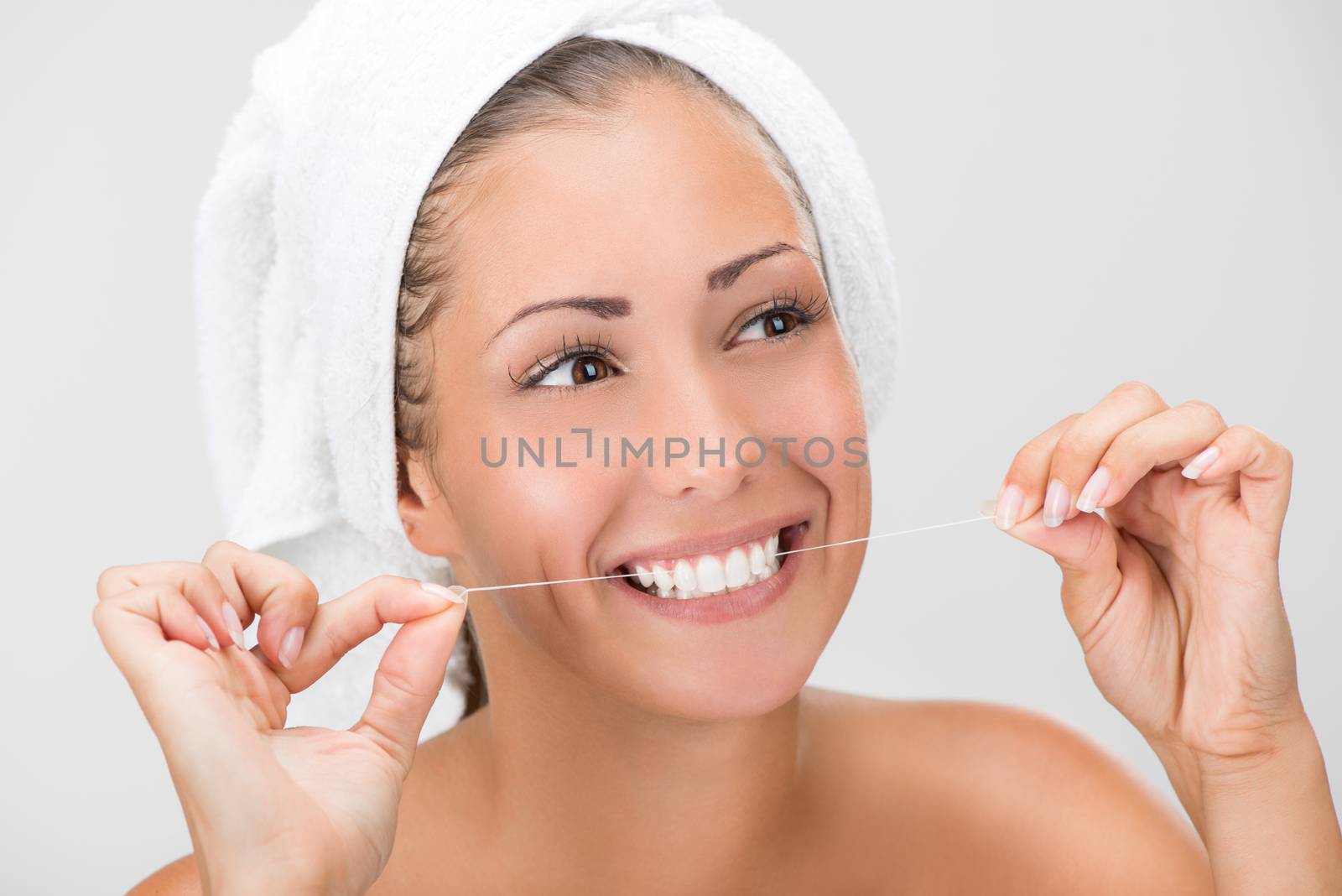 Cute girl preparing to start her day. She is cleaning teeth with dental floss. Looking at camera and smiling.