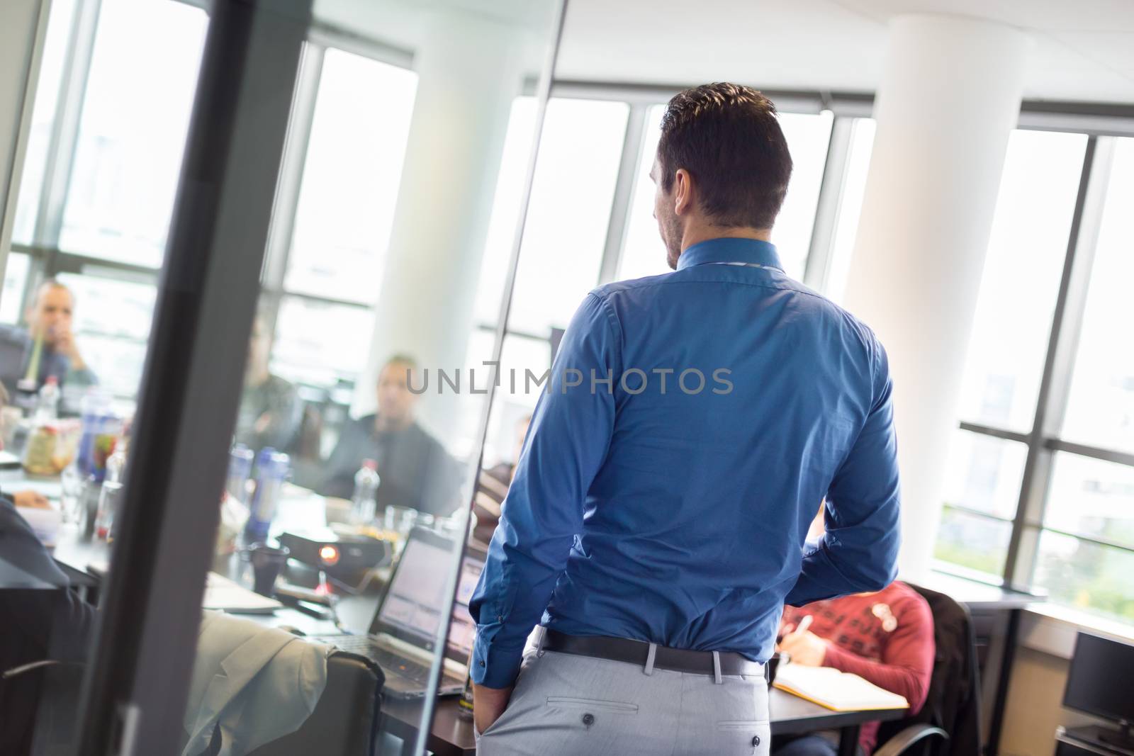 Business man making a presentation at office. Business executive delivering a presentation to his colleagues during meeting or in-house business training. View through glass.