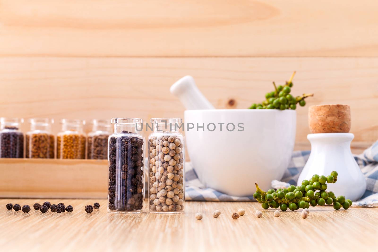 Assorted of spice bottles condiment black pepper ,white pepper and  green pepper seeds with mortar on wooden background.