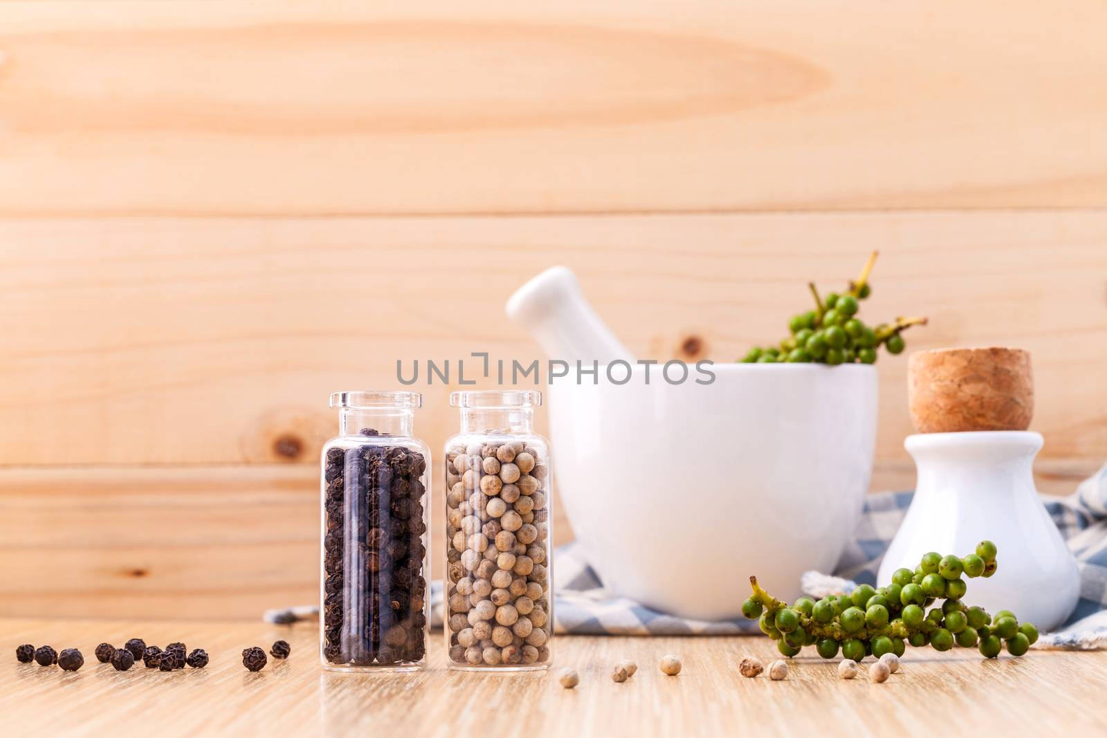 Assorted of spice bottles condiment black pepper ,white pepper and  green pepper seeds with mortar on wooden background.