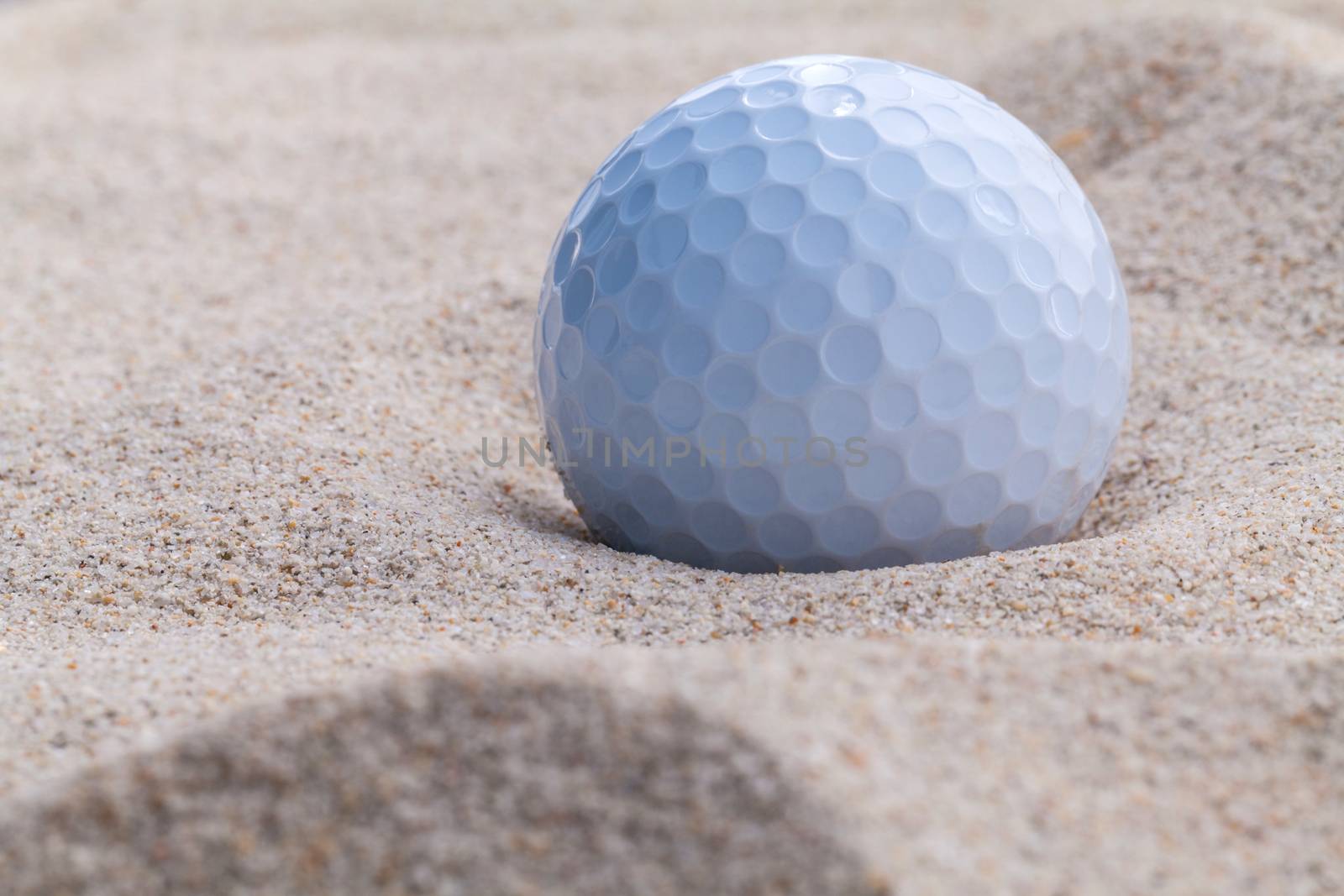 Close up golf ball in sand bunker shallow depth of field.