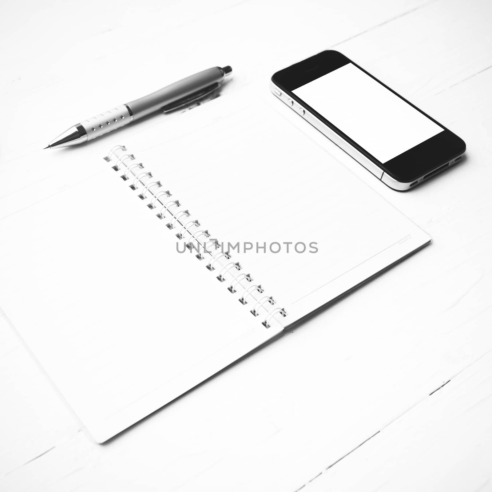 cellphone with notepad and pen over white table black and white color style