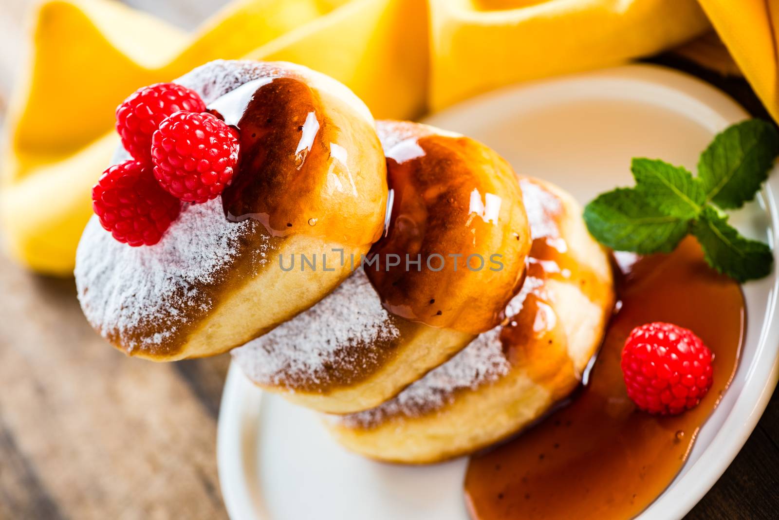 A stack of tree delicious german doughnuts powdered with sugar decorated with raspberry and raspberry sauce on white plate and yellow napkin