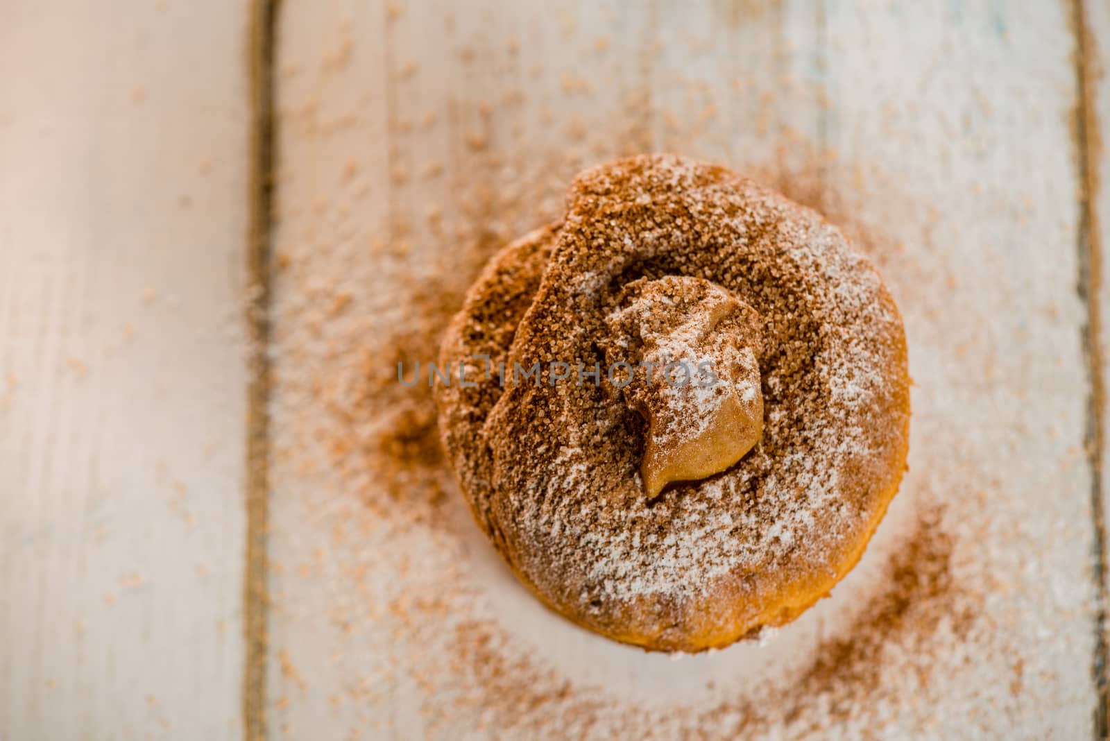 Top view of a small apple cake powdered with cinnamon and sugar on white wood table