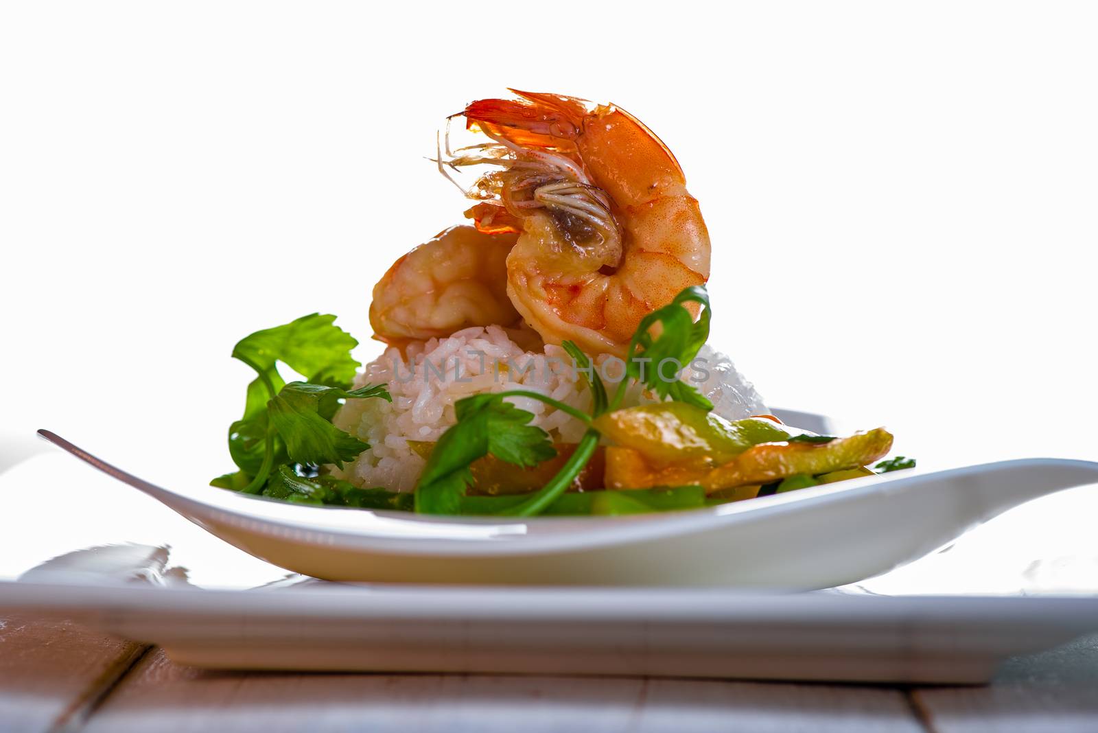 Dish with shrimps rice and green asparagus in a white plate, white background and white wood table