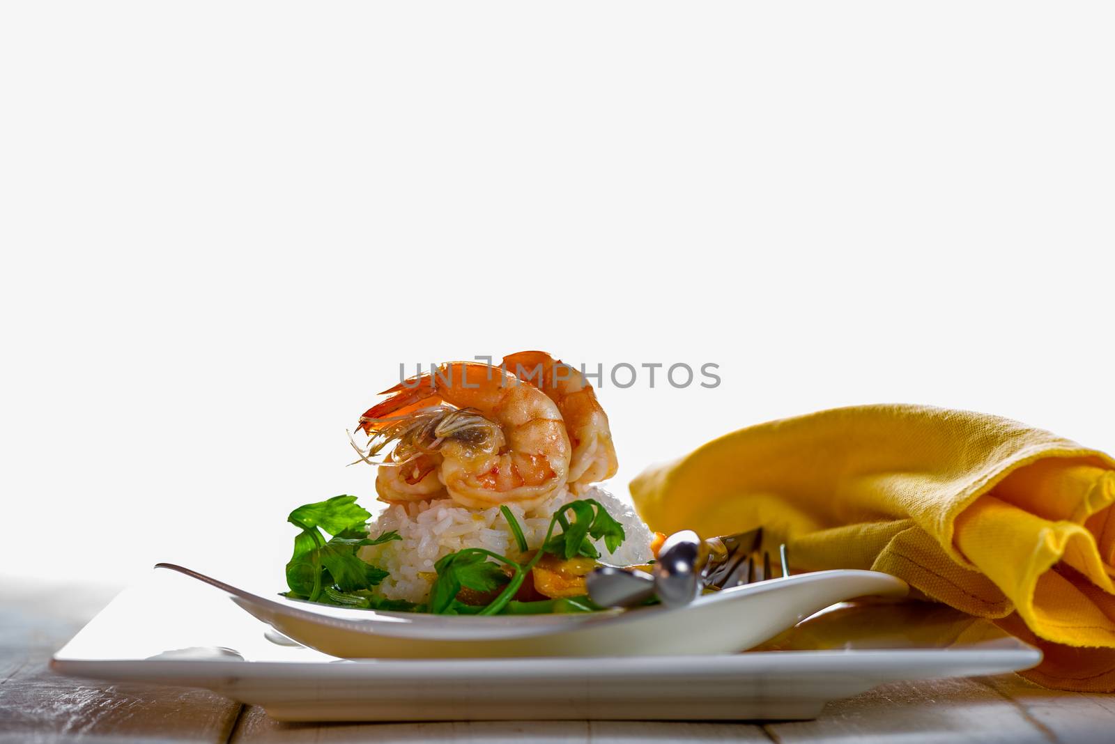 Dish with shrimps rice and green asparagus in a white plate, white background and white wood table