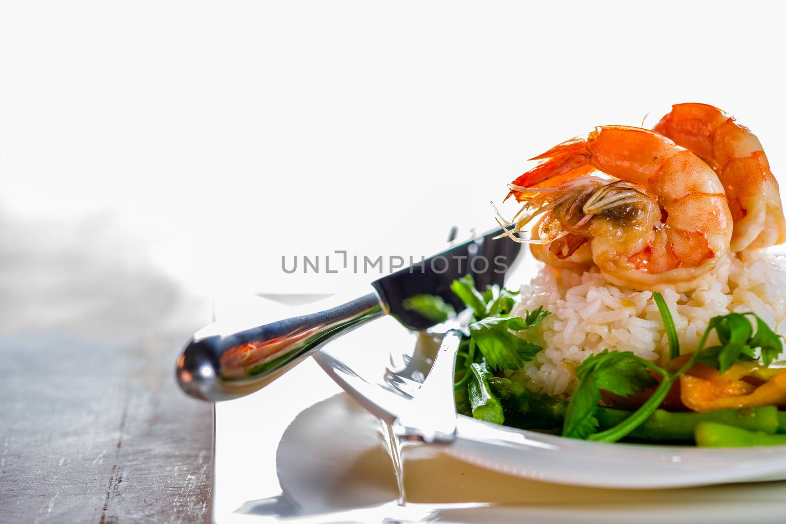 Dish with shrimps rice and green asparagus in a white plate, white background and white wood table