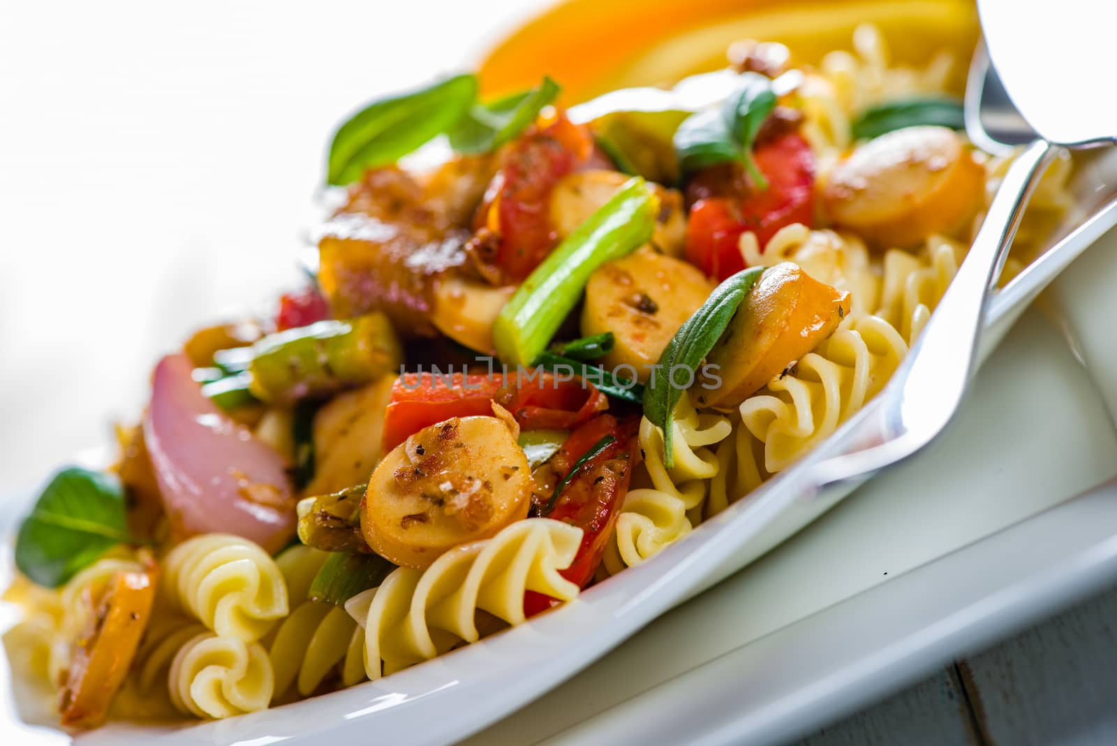 White pasta plate with vegetables and sausage on white background