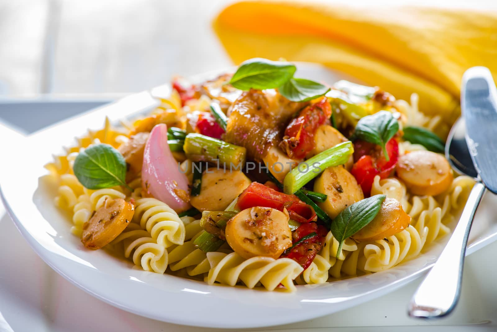 White pasta plate with vegetables and sausage on white background