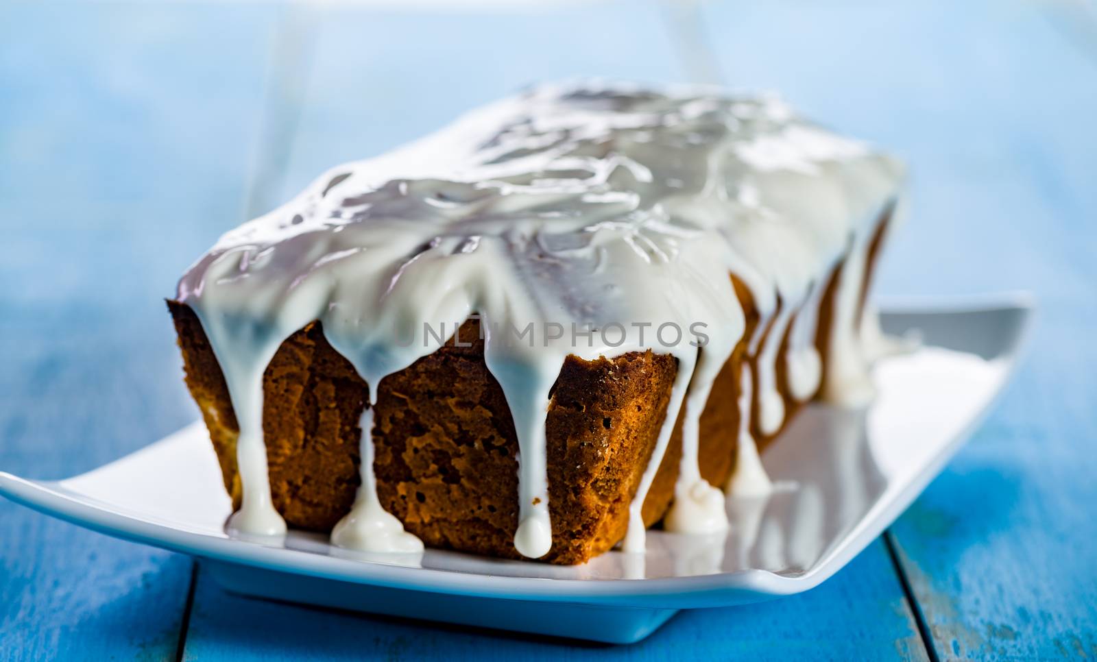 loaf cake with icing on white plate and blue wood table