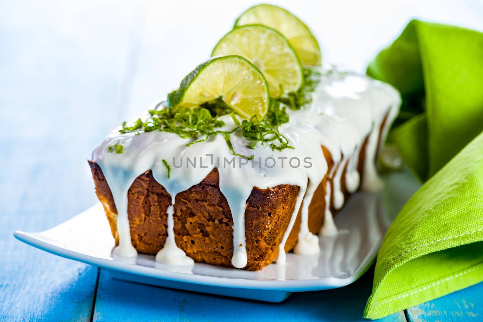 lemon loaf cake with icing decorating with lemon on white plate and blue wood table