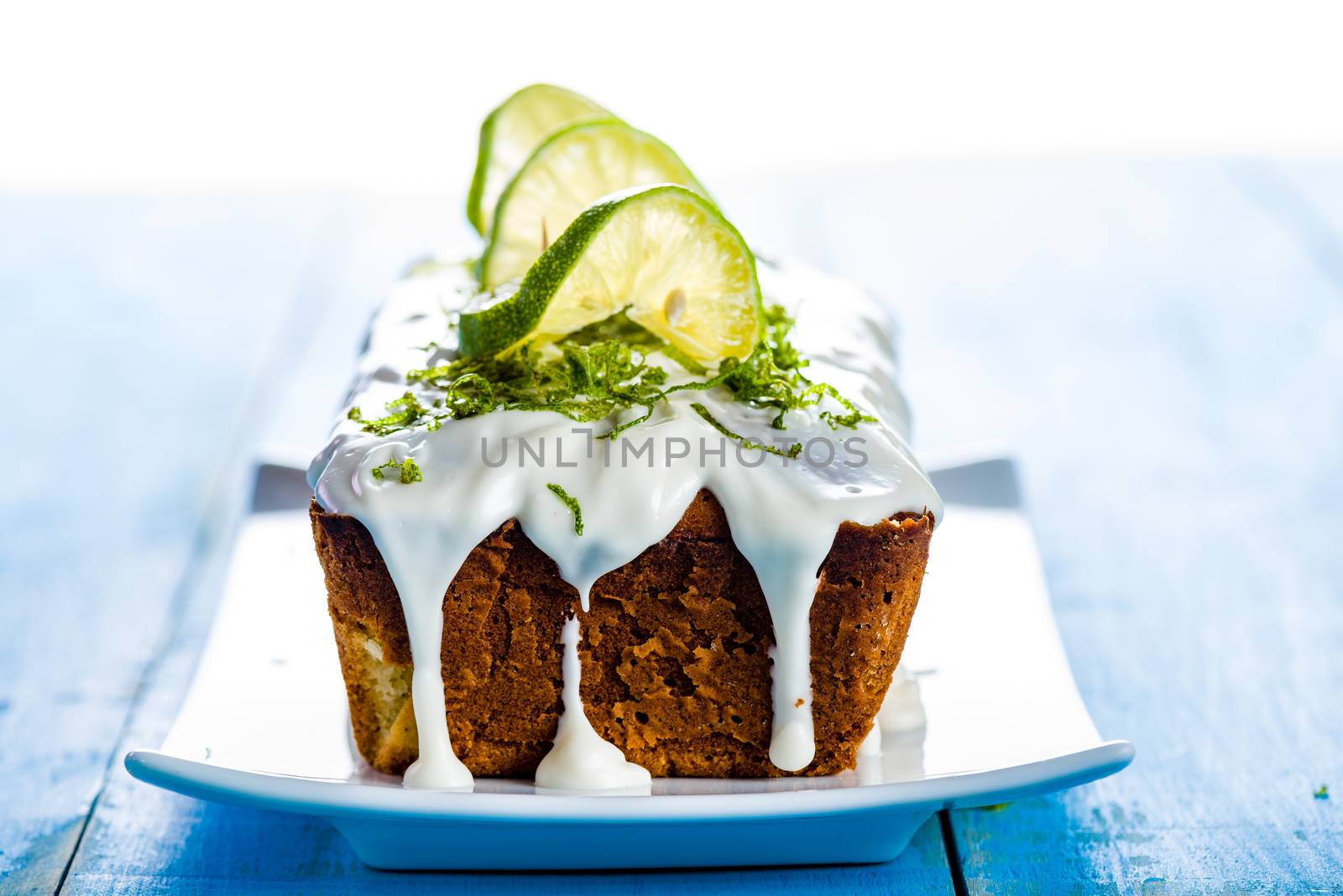 lemon loaf cake with icing decorating with lemon on white plate and blue wood table