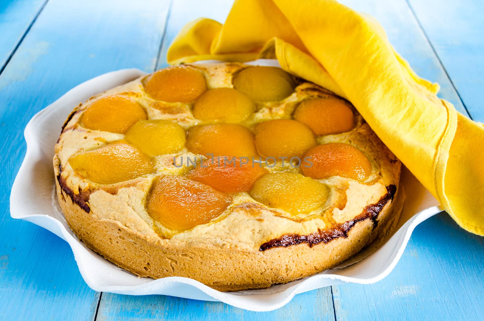 Homemade fresh apricot cake on blue wood table with yellow napkin