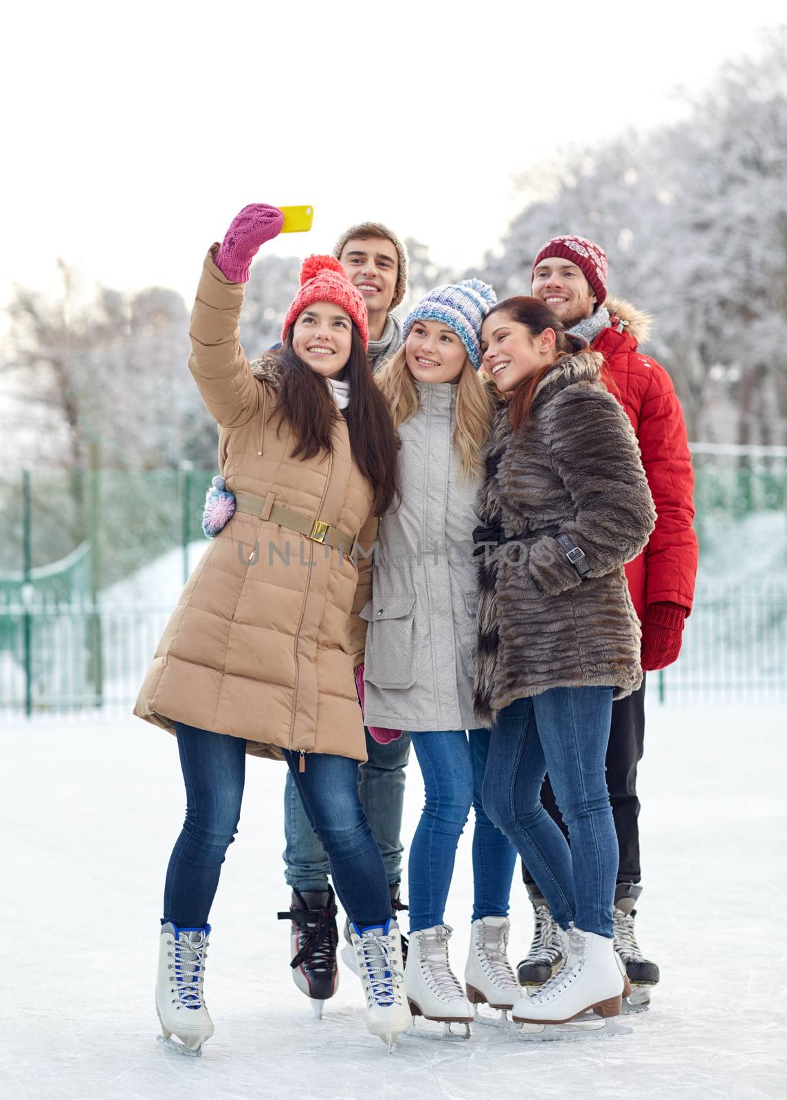 happy friends with smartphone on ice skating rink by dolgachov