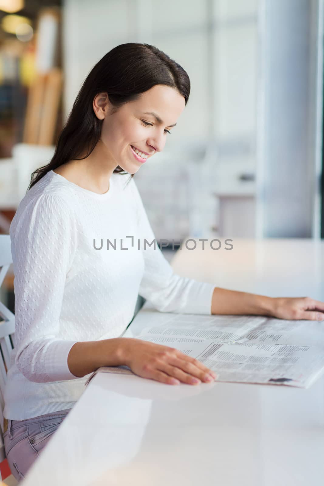 leisure, information, mass media, people and lifestyle concept - smiling young woman reading newspaper at cafe