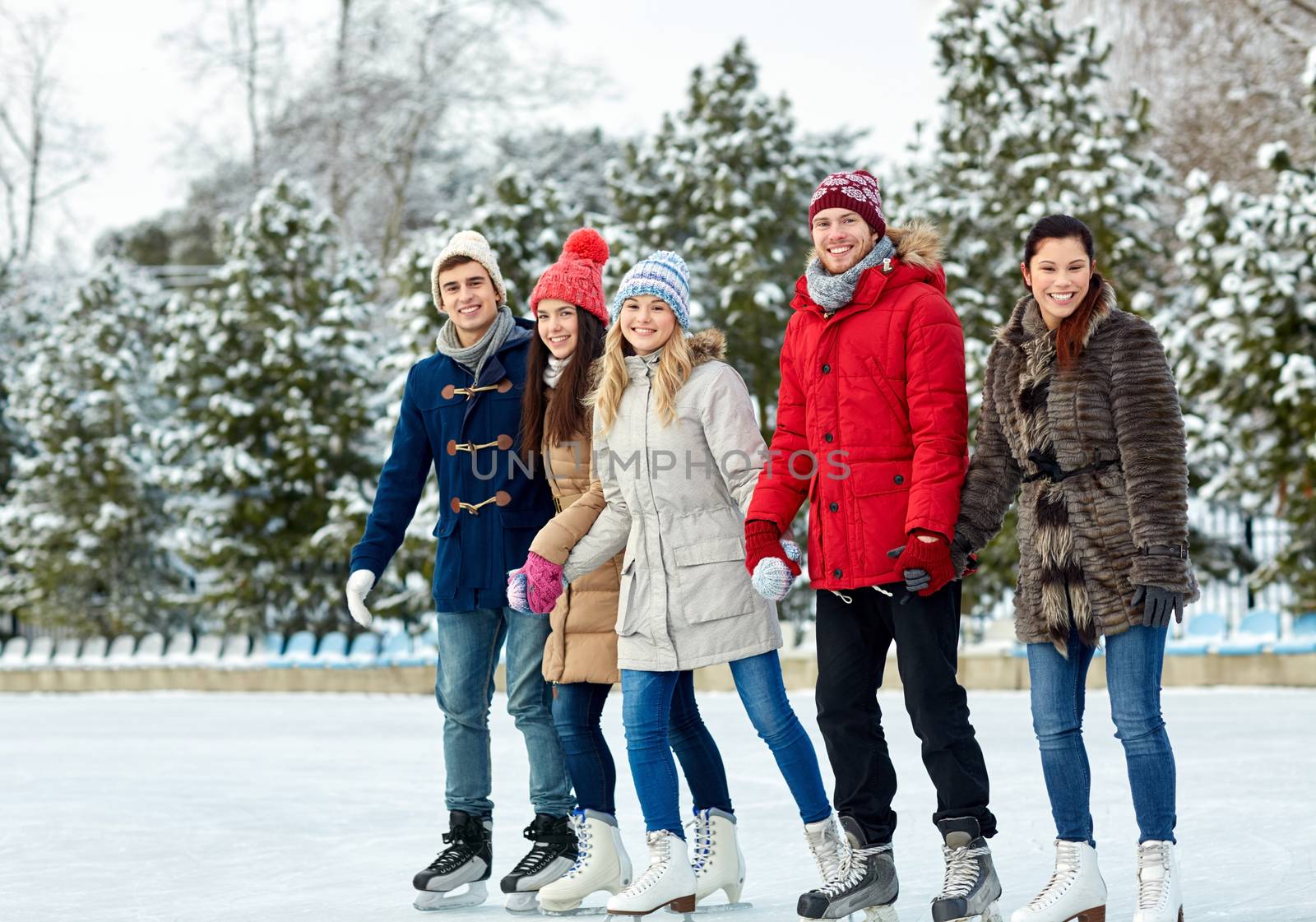 happy friends ice skating on rink outdoors by dolgachov