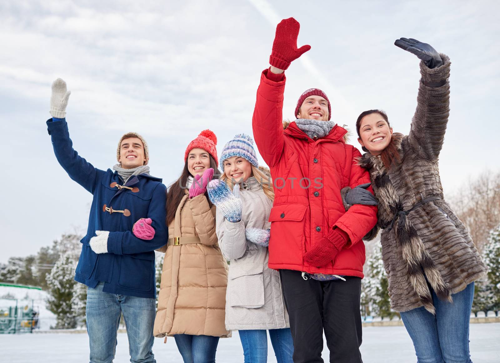 happy friends waving hands on ice rink outdoors by dolgachov