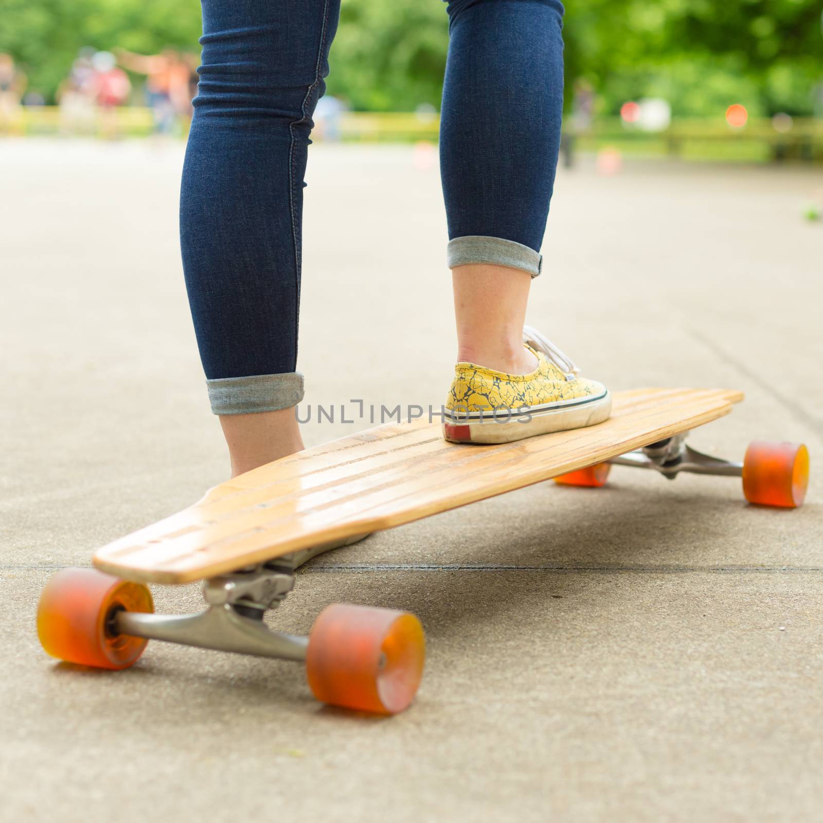 Teenage girl wearing blue jeans and sneakers practicing long board riding in skateboarding park. Active urban life. Urban subculture.