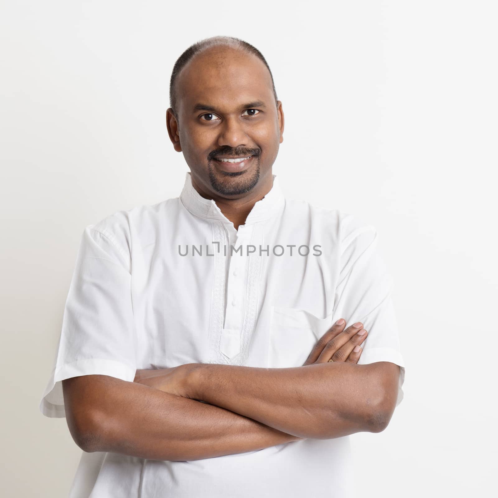Portrait of mature casual business Indian man smiling, standing on plain background with shadow.