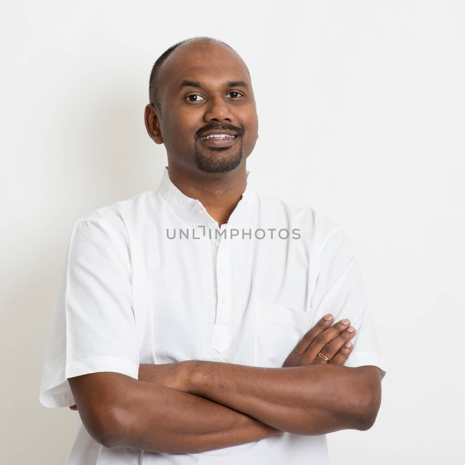 Portrait of happy mature casual business Indian man, standing on plain background with shadow.