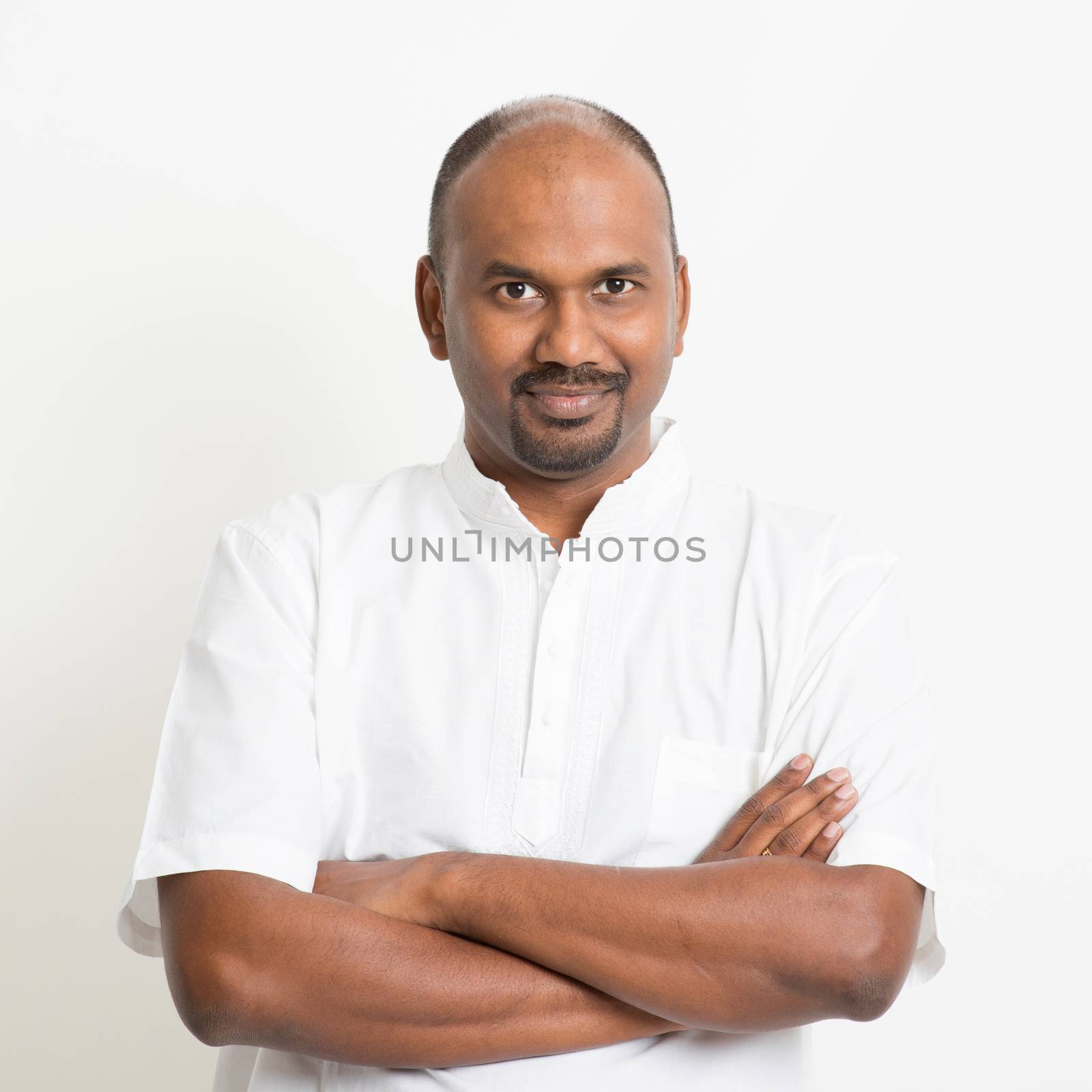 Portrait of mature casual business Indian man arms crossed, standing on plain background with shadow.