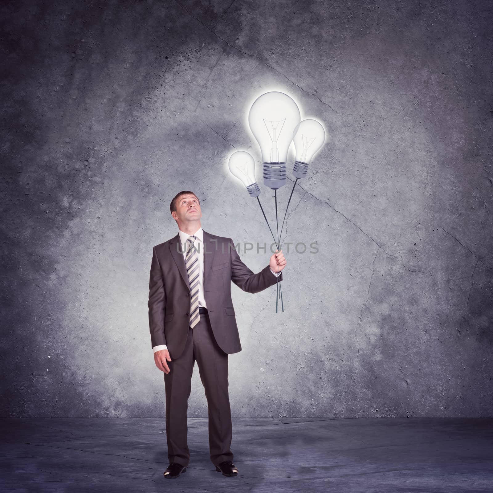 Businessman holding set of big bulbs on grey wall background
