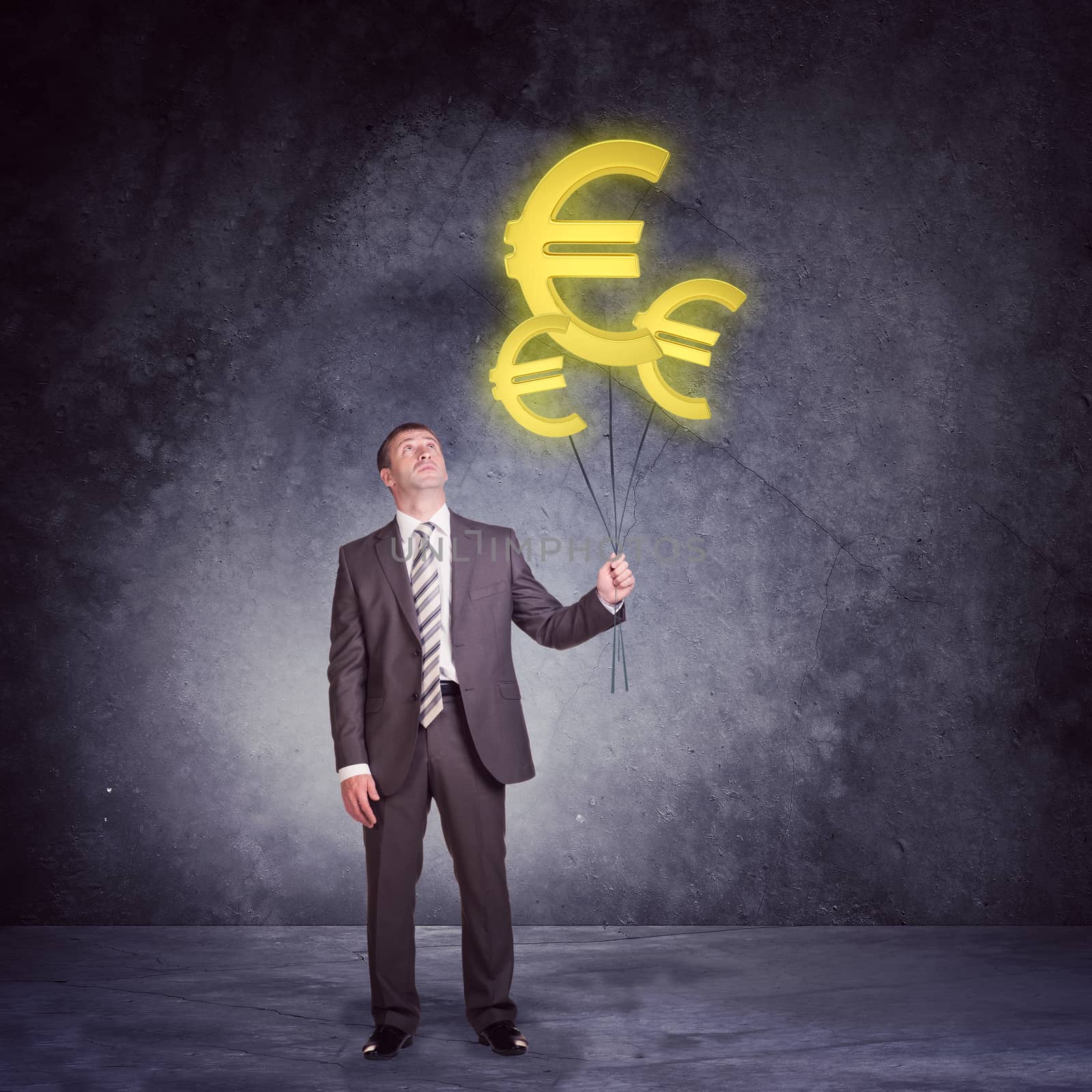Businessman holding set of big euro signs on grey wall background