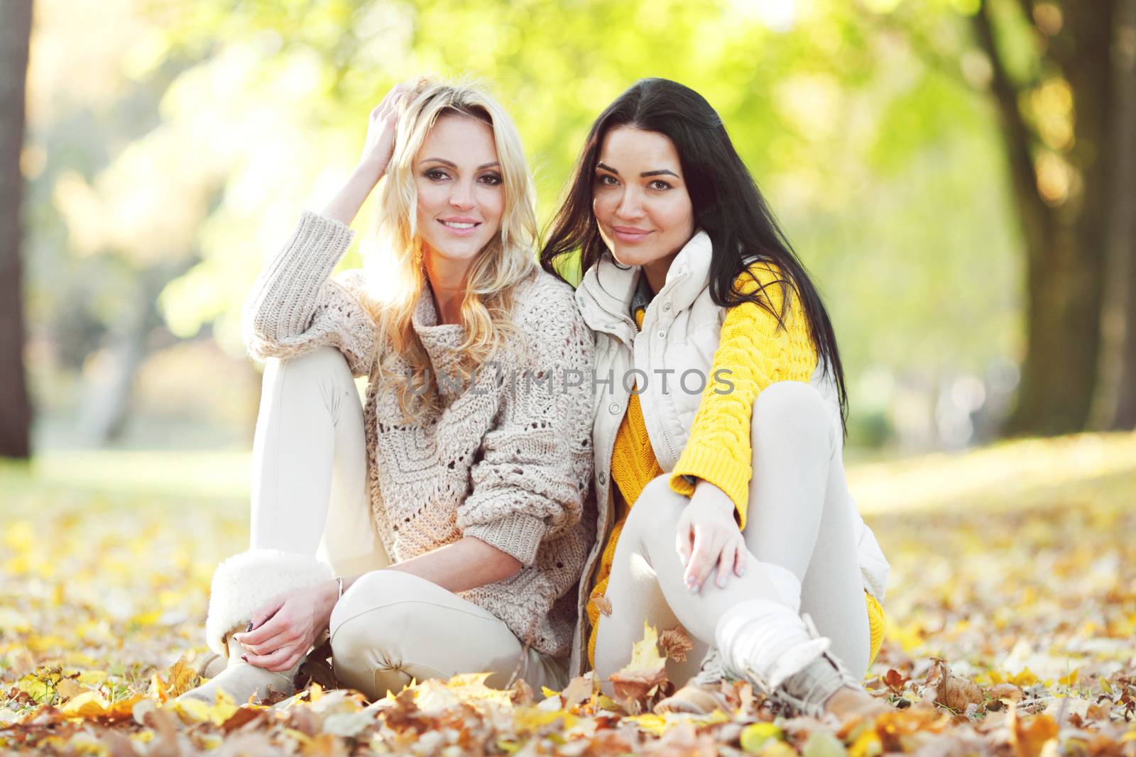 Happy female friends sitting on ground in autumn park