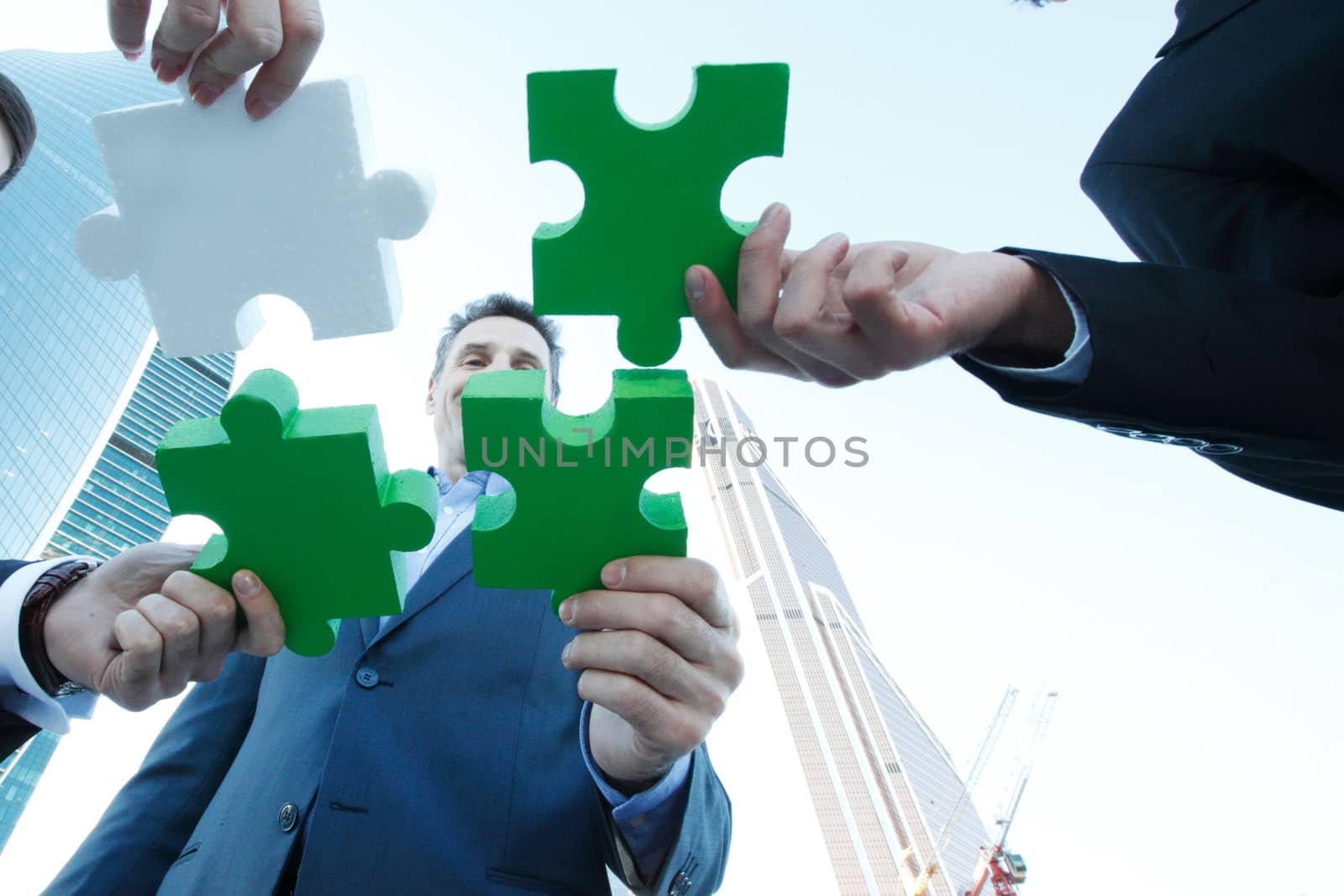 Business people assembling jigsaw puzzle near skyscrapers